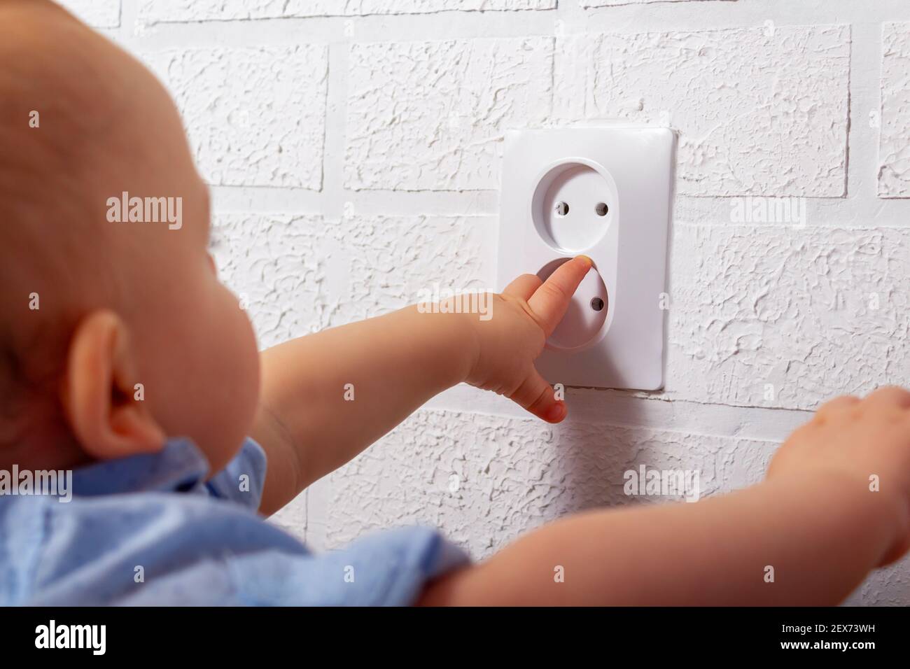 Un garçon caucasien méconnaissable joue avec une prise électrique ouverte. Fils pour bébés. Jeux dangereux avec prise électrique ouverte. Banque D'Images