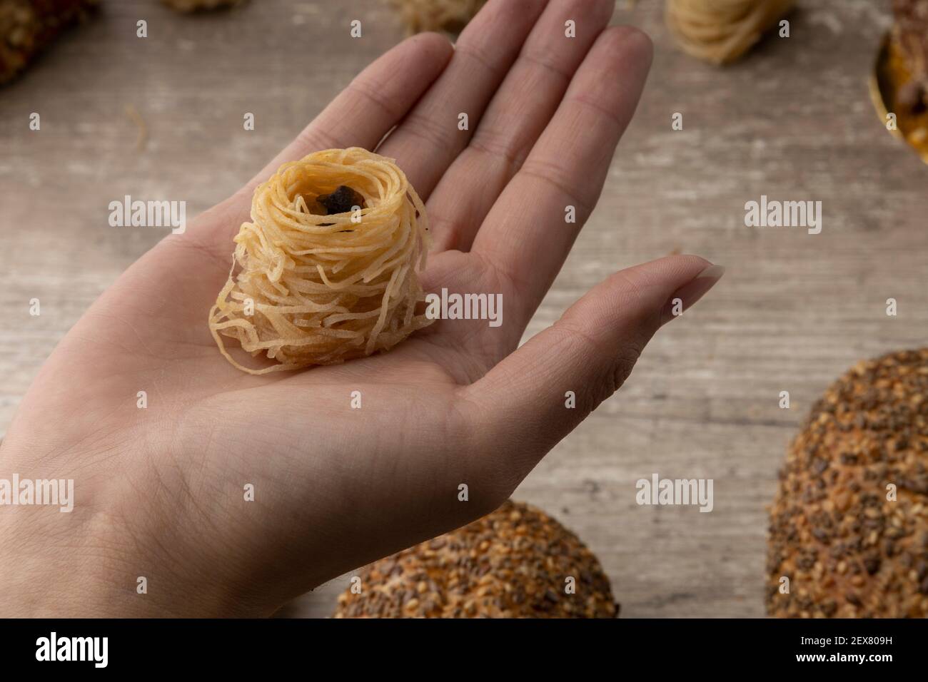 la paume d'une main tenant un dessert arabe en forme de nid avec noix à l'intérieur, fond en bois et pains, studio Banque D'Images