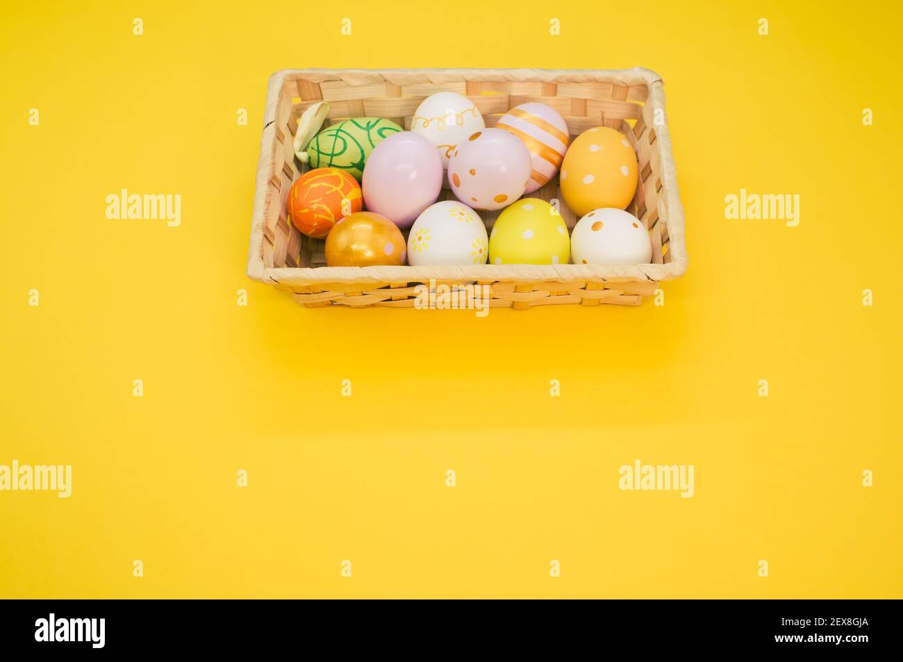 Un panier tissé rempli d'œufs de Pâques colorés sur jaune arrière-plan Banque D'Images