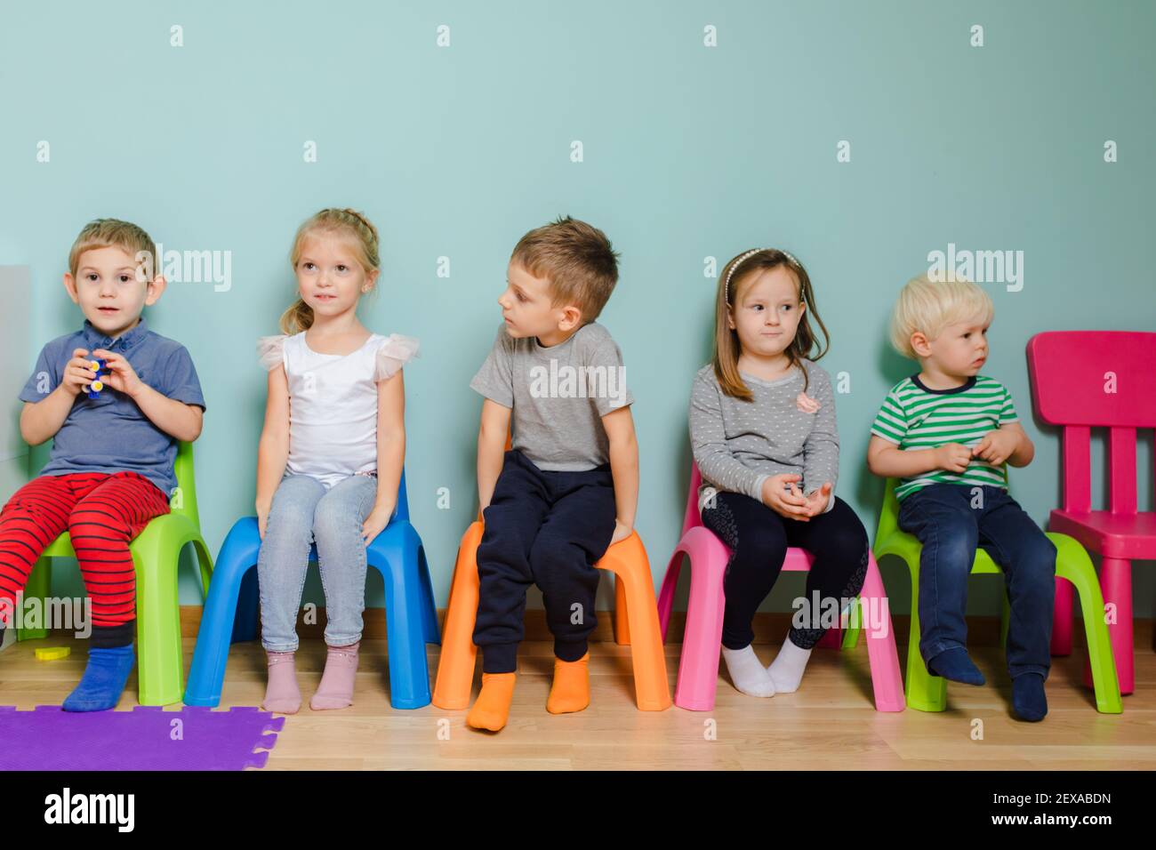 Les enfants sont assis sur les chaises colorées de la maternelle Banque D'Images