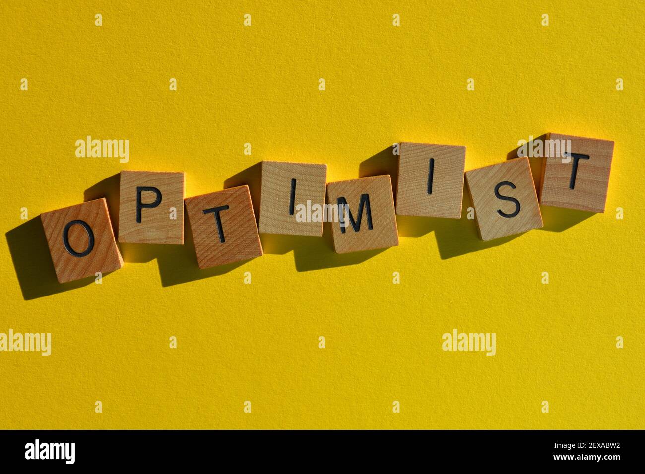 Optimiste, mot en lettres de l'alphabet de bois isolées sur fond jaune vif Banque D'Images