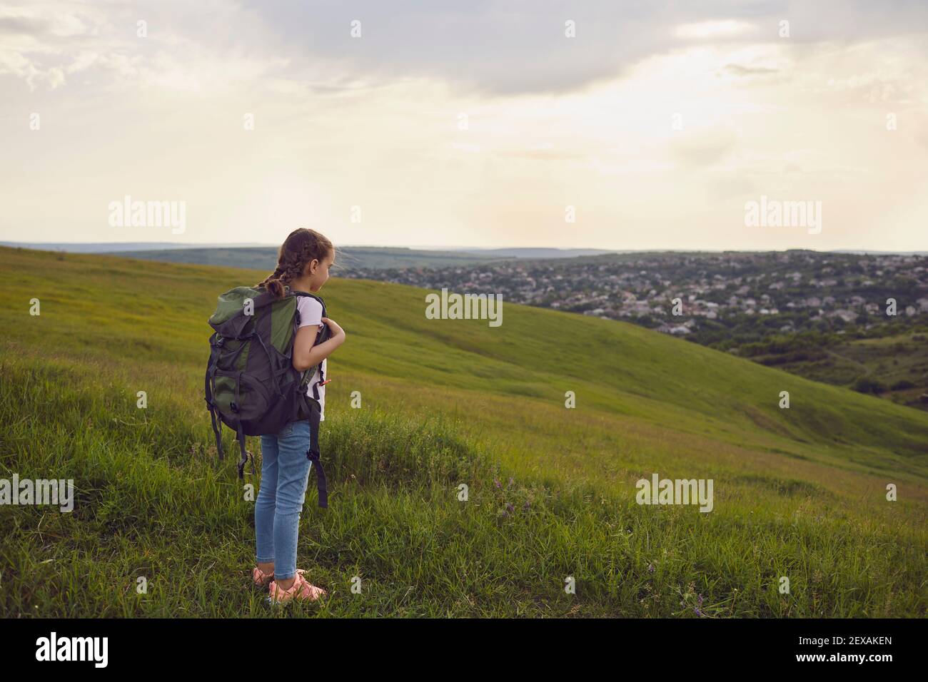 Une petite randonneur touristique avec des sacs à dos regarde le coucher de soleil sur une colline en été. Petite fille sur pied voyage aventure dans la nature Banque D'Images