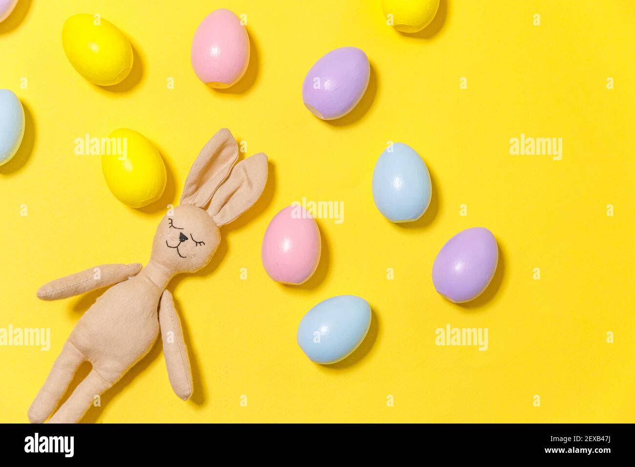 Concept joyeuses Pâques. Préparation pour les vacances. Œufs de pâques colorés et jouet de lapin isolé sur fond jaune tendance. Espace de copie de la vue de dessus de la pose à plat simple et minimaliste Banque D'Images