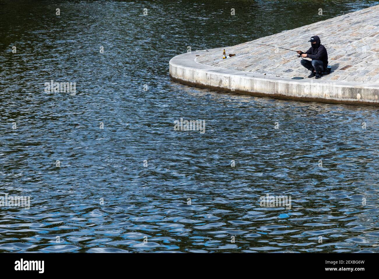 Homme assis sur une petite côte en béton près de la rivière et de la pêche Banque D'Images