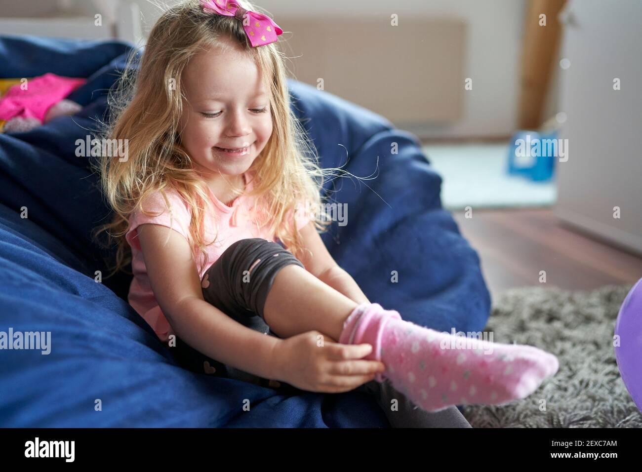 Bonne petite fille assise dans le sac et la mettant chaussettes roses Banque D'Images