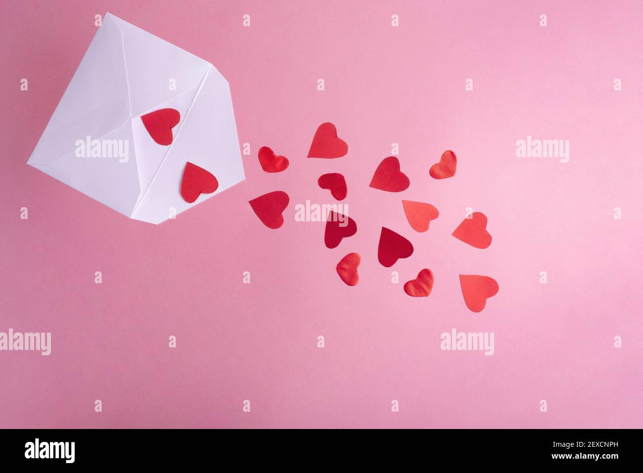 Cœur rouge volant d'une enveloppe blanche sur fond rose, gros plan. Carte de Saint-Valentin. Banque D'Images