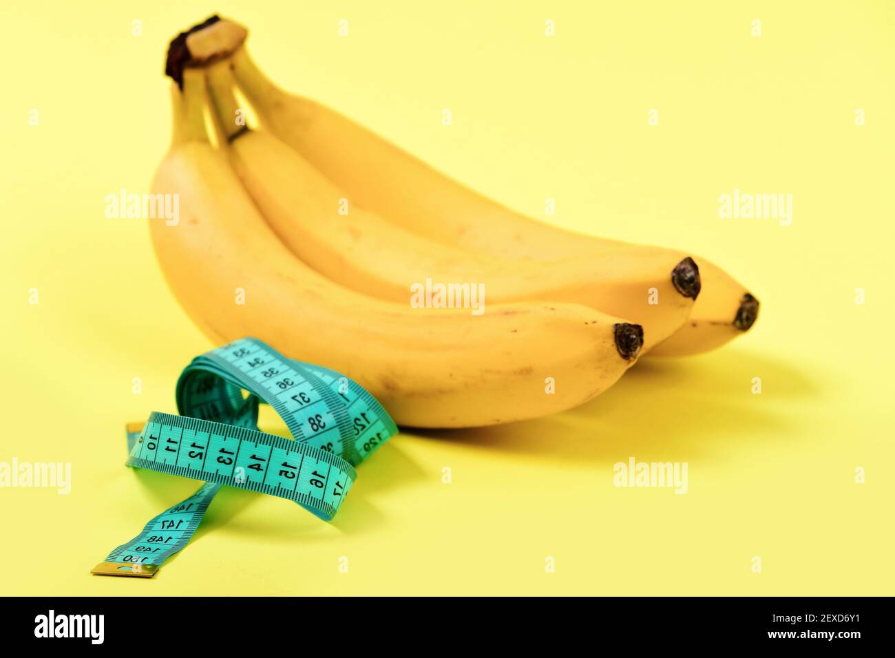 Pour la mesure de bande de couleur turquoise à côté de tas de bananes, isolé sur fond jaune clair. Concept de régime alimentaire faible en calories et vitamines alimentation Banque D'Images