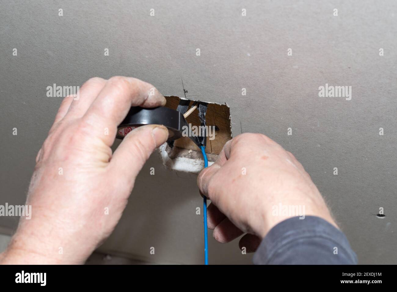 Un électricien isole les fils électriques torsadés dans une prise coupée dans la cloison sèche. Installation des communications. Banque D'Images