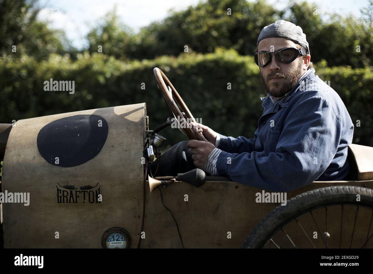 Voyage en voiture avec un homme de vélo d'époque Grafton avec chapeau et lunettes style vintage conduisant sur une route. Banque D'Images