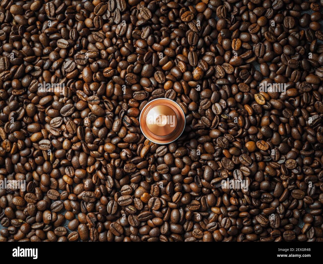 Une capsule espresso italien dorée recyclable sur une pile de grains de café torréfiés. Vue de dessus. Banque D'Images