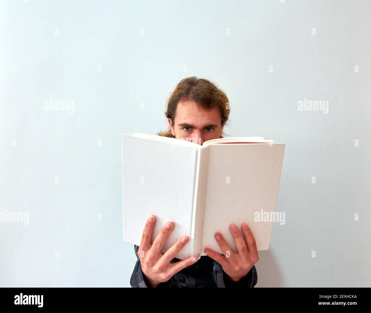 Un homme caucasien lisant un livre sur le fond de mur blanc Banque D'Images