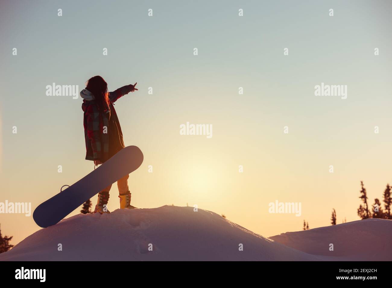 Jeune fille débutant snowboarder se tient à l'heure du coucher du soleil sur la montagne haut Banque D'Images