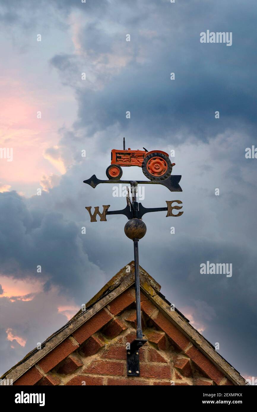 Les fermiers weathervane métal rouge vieux tracteur sur le toit de la grange montrant direction nord-est sud-ouest du vent avec le pointeur de flèche vers l'intérieur devant le ciel du coucher du soleil Banque D'Images