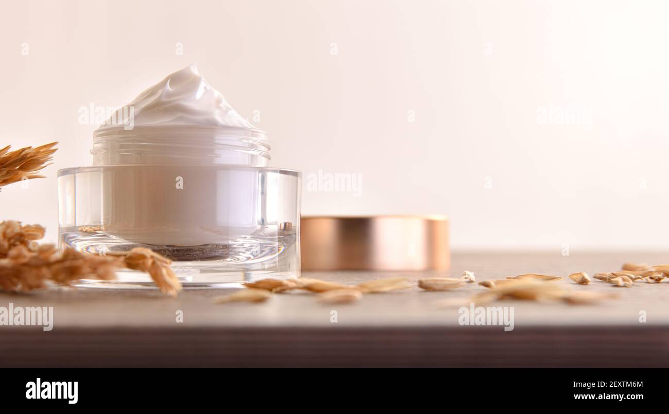 Crème hydratante pour le corps et le visage d'avoine dans un pot en verre avec pointes sur table en bois avec fond beige isolé Banque D'Images