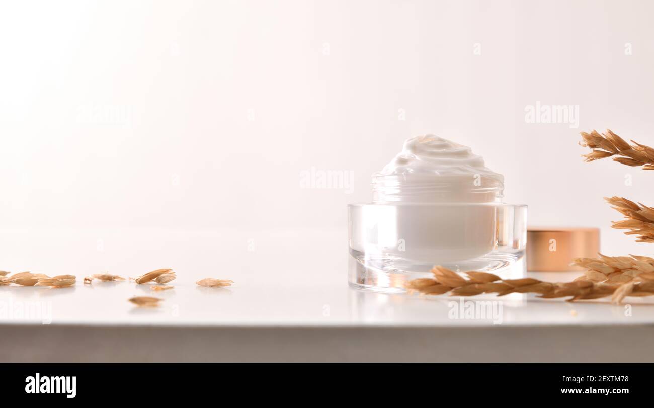 Crème hydratante pour le corps et le visage d'avoine dans un pot en verre avec pointes sur table en bois avec fond blanc isolé Banque D'Images