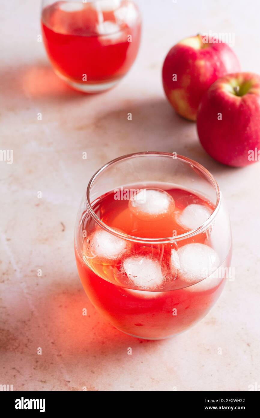 Deux verres de boisson aux pommes Pink Lady avec glaçons et deux pommes fraîches en arrière-plan. Banque D'Images