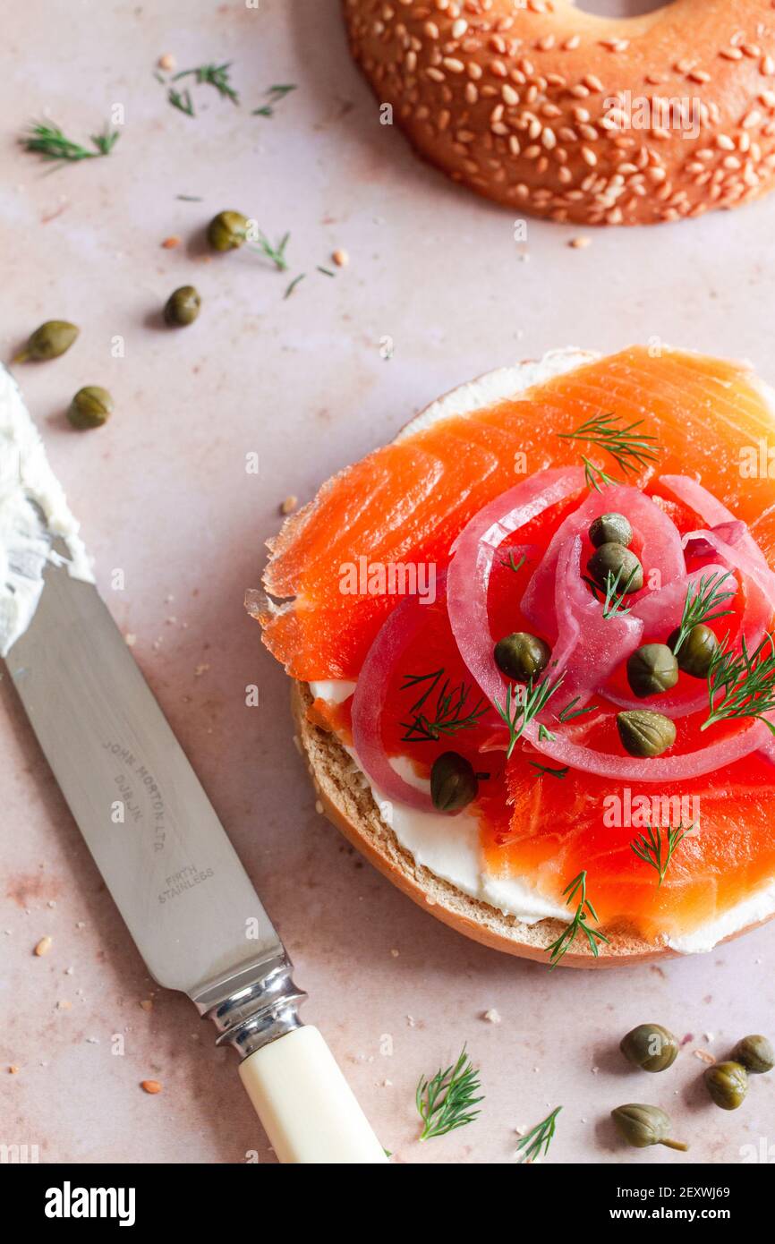 Bagel à moitié étalé avec fromage à la crème et recouvert de truite fumée, d'oignon rouge mariné, de câpres et d'aneth. Banque D'Images