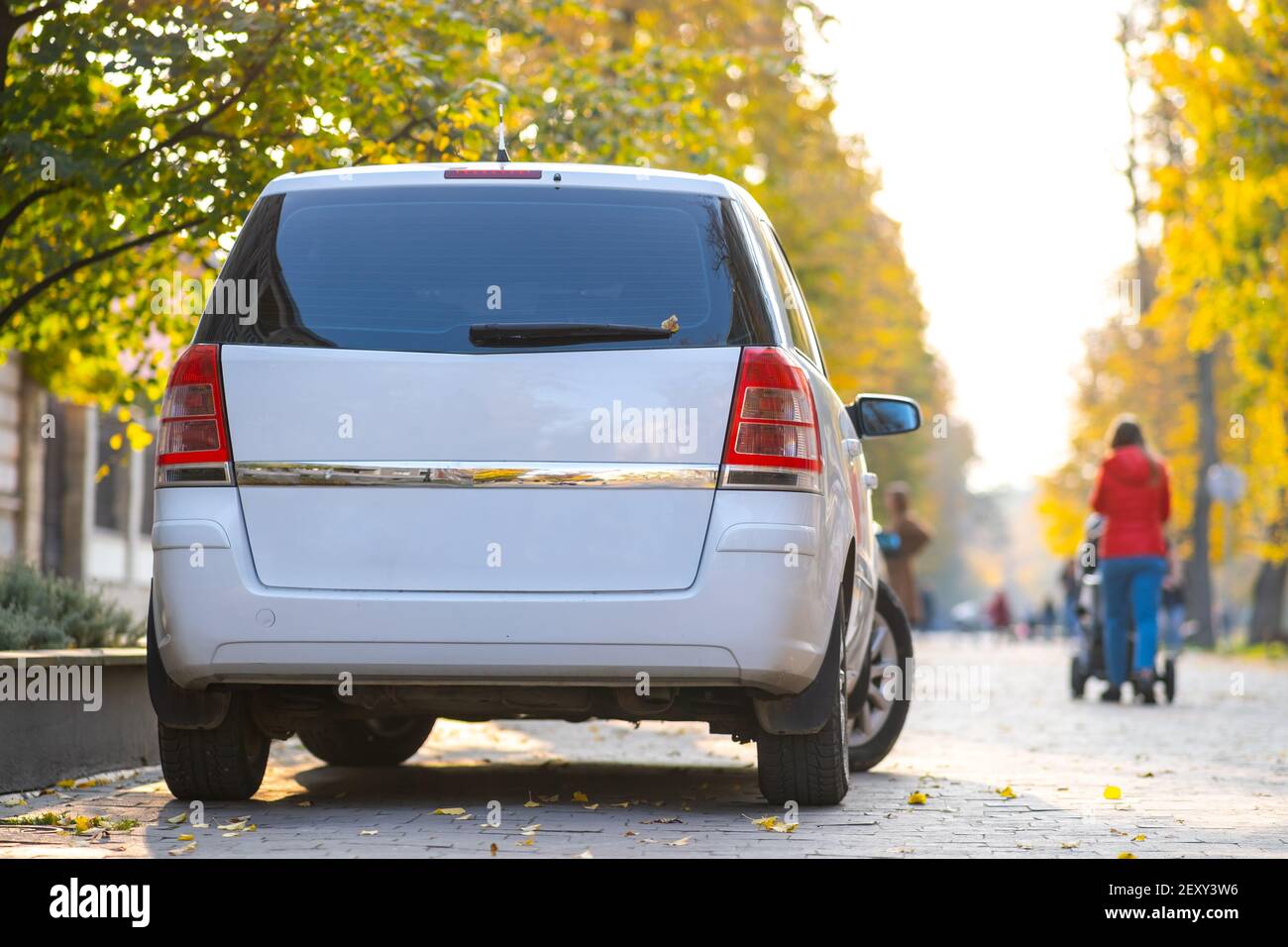 Voitures garées dans une rangée sur le côté de la rue de la ville le jour d'automne lumineux avec des personnes floues marchant sur la zone piétonne. Banque D'Images