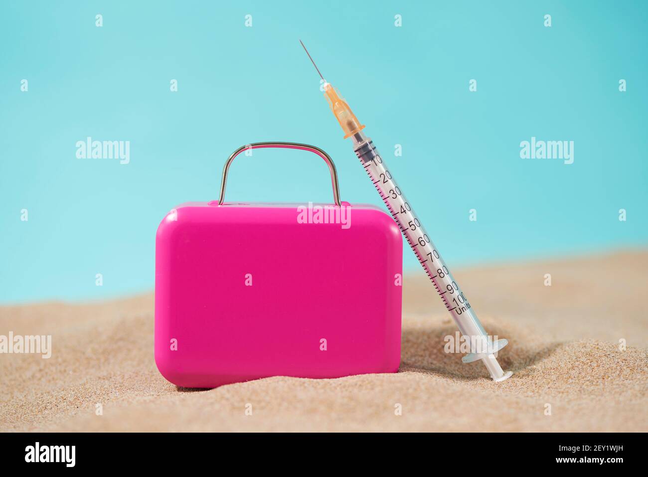 une seringue et une valise rose sur le sable, sur fond bleu, représentant le tourisme médical Banque D'Images