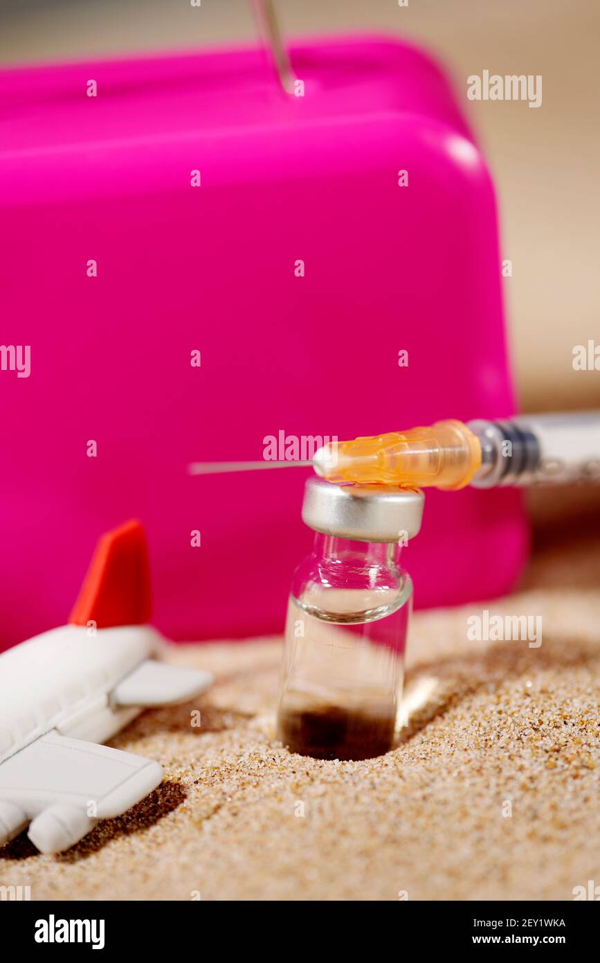 gros plan d'une seringue, d'un flacon, d'un avion et d'une valise rose sur le sable, représentant le tourisme médical Banque D'Images