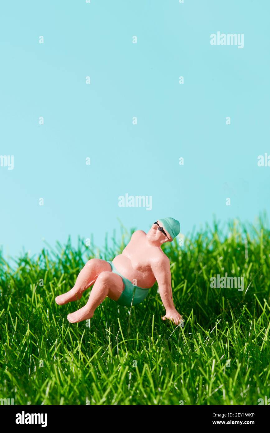 gros plan d'un homme miniature en maillot de bain reposant sur l'herbe, sur un fond bleu avec un peu d'espace sur le dessus Banque D'Images