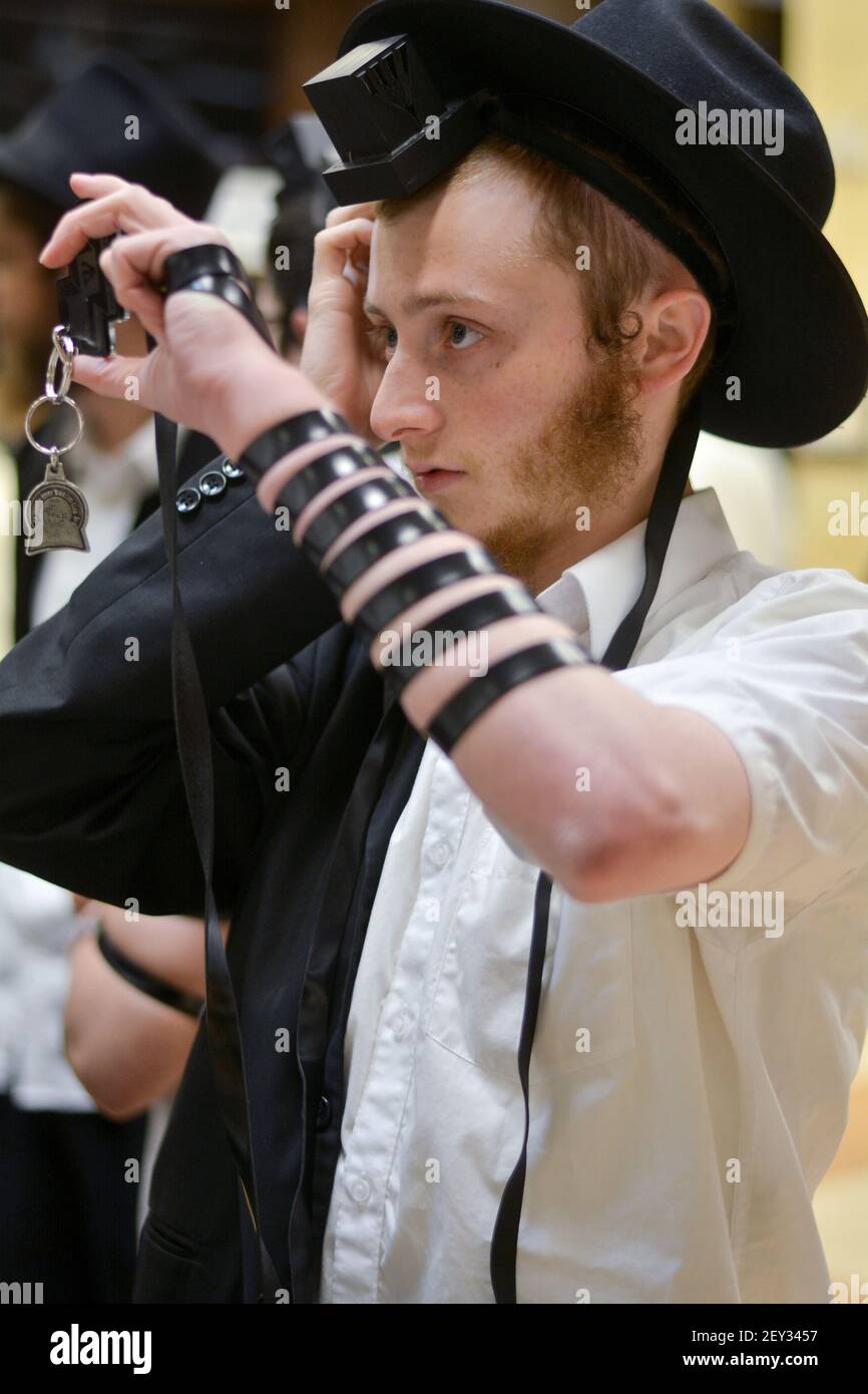 Un jeune juif met sa tefiline (phylactères) dans une synagogue de Chabad à Crown Heights, Brooklyn, New York. Banque D'Images