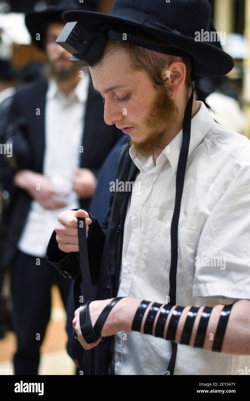 Un jeune juif met sa tefiline (phylactères) dans une synagogue de Chabad à Crown Heights, Brooklyn, New York. Banque D'Images