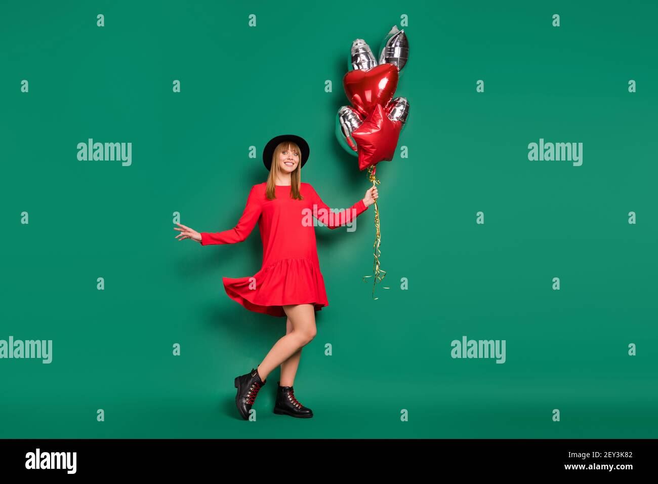 Photo de jolie dame regarder caméra tenir air ballons usure chapeau rouge robe bottes isolé vert fond Banque D'Images