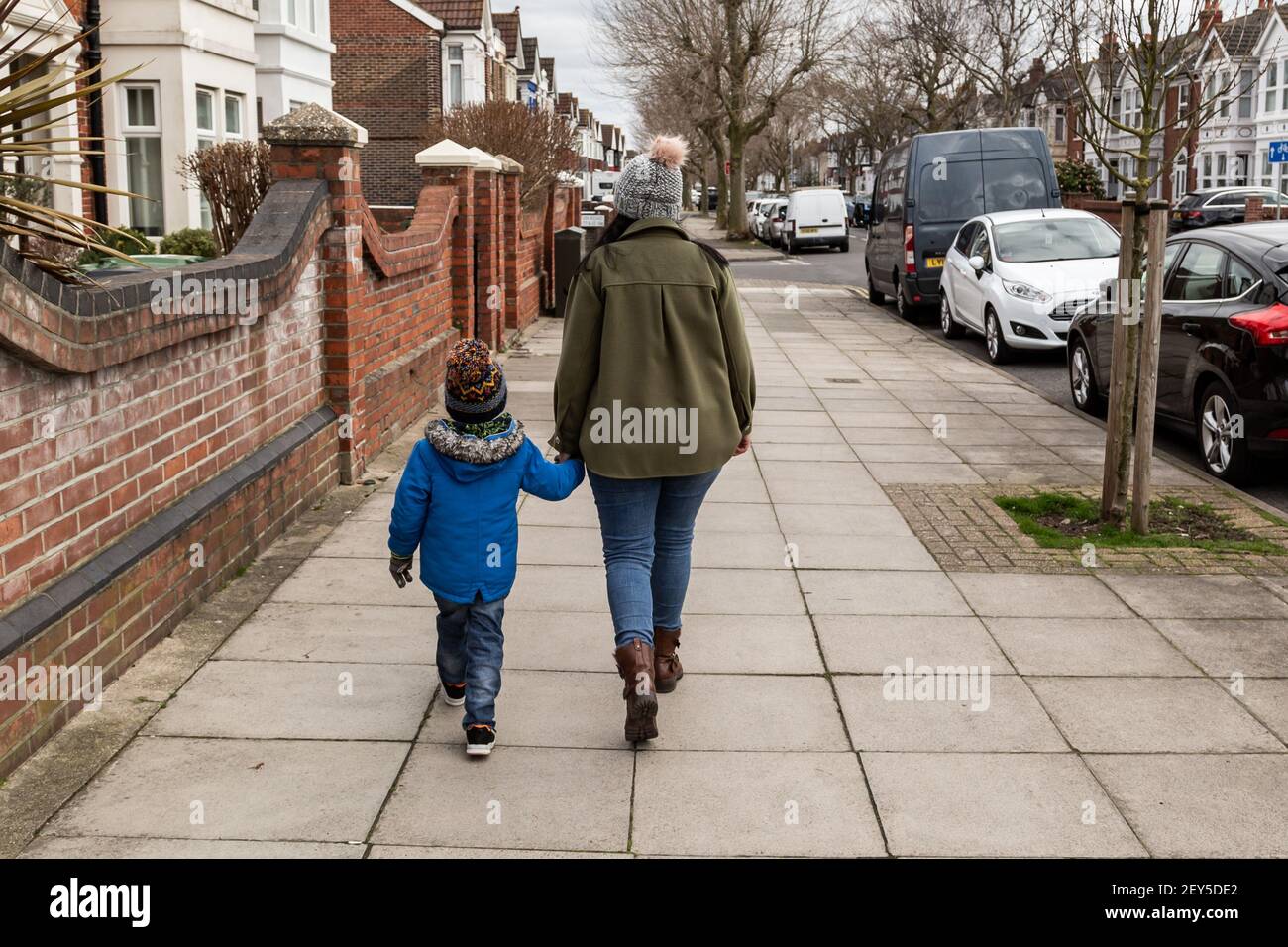 Une mère et un fils marchant sur le trottoir en tenant les mains prise de vue de derrière Banque D'Images
