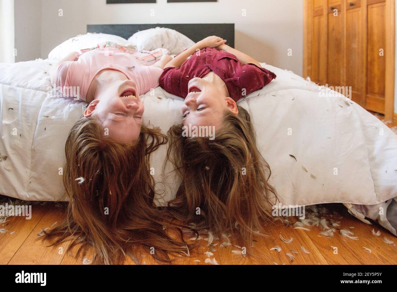 Deux jeunes filles heureuses ayant un oreiller en plumes se battent sur le lit. Banque D'Images
