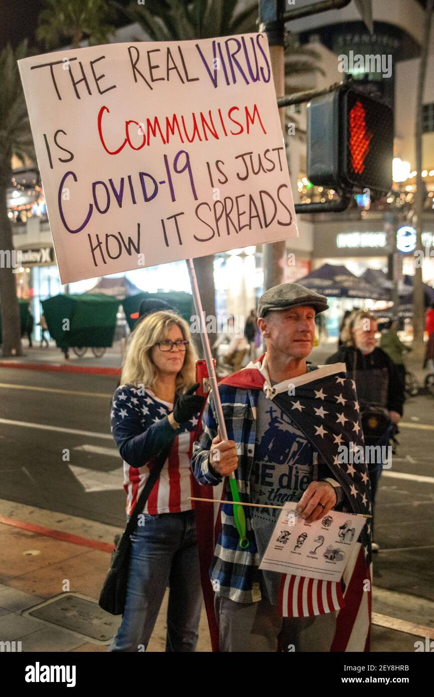 Un manifestant à Huntington Beach, en Californie, qui porte le drapeau américain, assimile illogiquement le communisme à la pandémie COVID-19. Banque D'Images