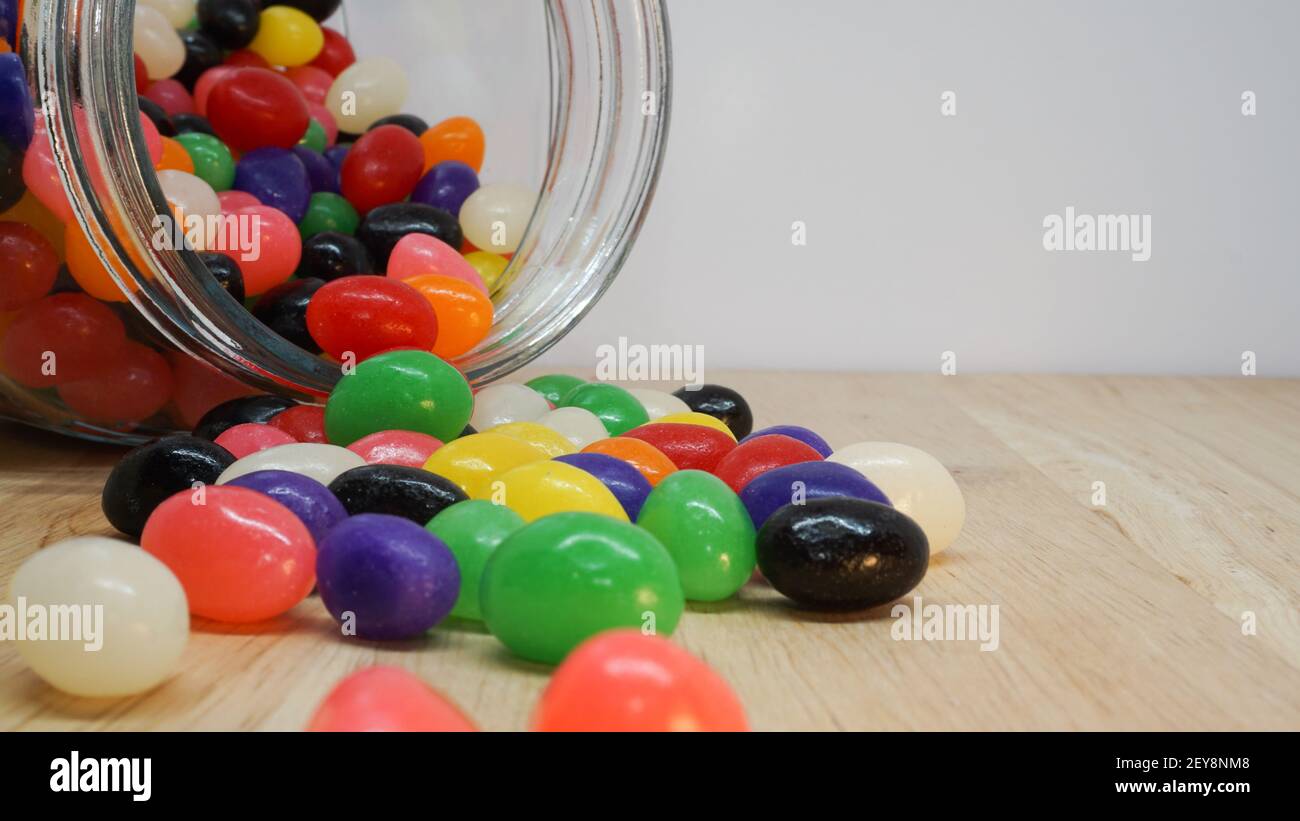 Des jelly beans colorés débordent d'un pot en verre sur la table. Espace blanc dans le coin supérieur du message Banque D'Images