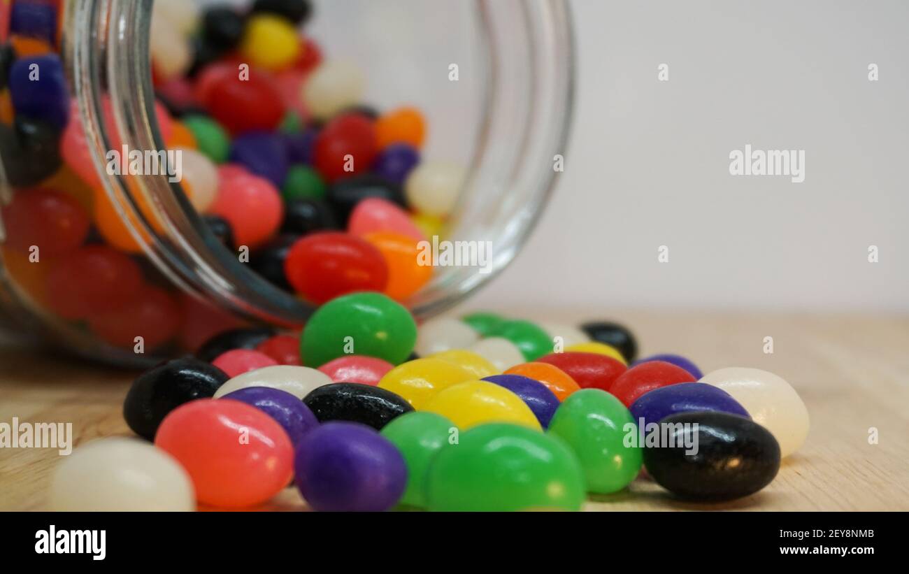 Des jelly beans colorés débordent d'un pot en verre sur la table. Espace blanc dans le coin supérieur du message Banque D'Images