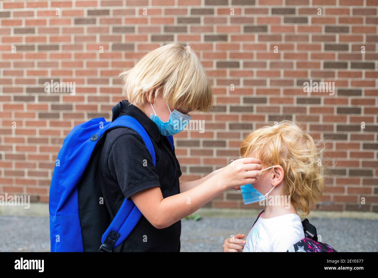 Les enfants dans les masques. Concept de retour à l'école après réouverture. Un écolier met un masque sur sa petite sœur pendant l'épidémie de virus corona. Les petits enfants portent un revers Banque D'Images