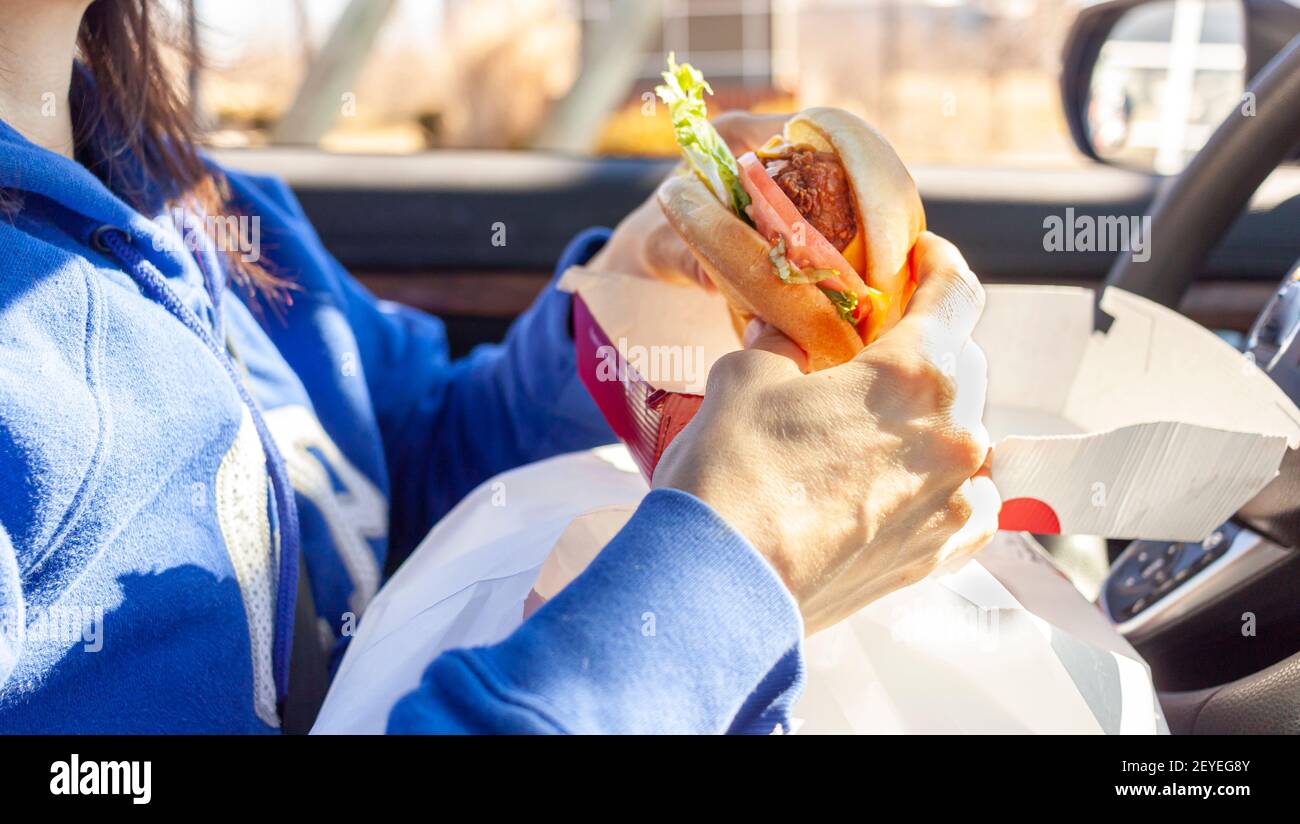 Une femme mange un sandwich de poulet qu'elle a obtenu d'un trajet de route à travers la chaîne de restauration rapide. Elle a des paquets de nourriture sur ses genoux alors qu'elle mange dans le dr Banque D'Images