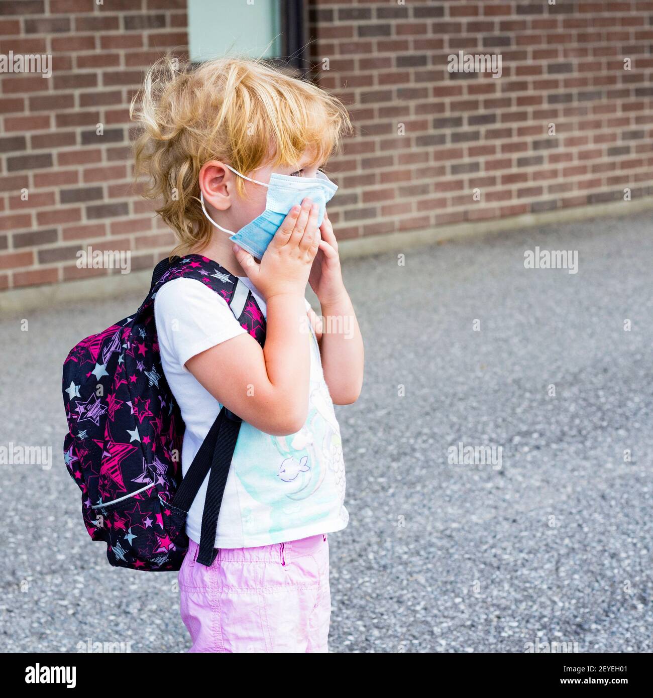 Petit enfant d'âge préscolaire dans le masque avec sac à dos pendant le virus corona près du bâtiment de l'école, aller à l'école ou à la maternelle. Premier jour à l'école concept. Banque D'Images