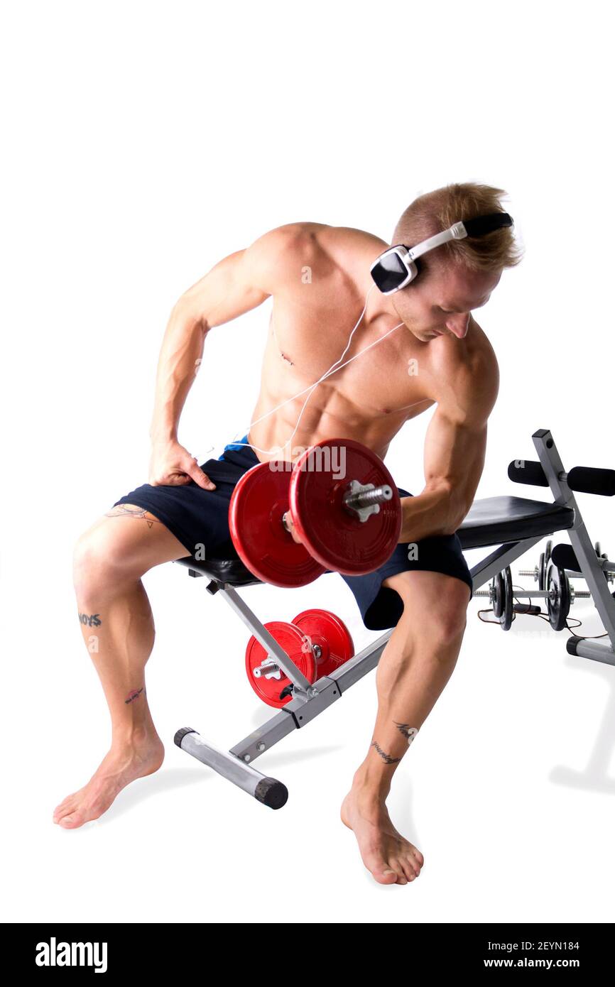 Un jeune homme blond musclé qui soulève des poids et écoute de la musique dans un casque Banque D'Images