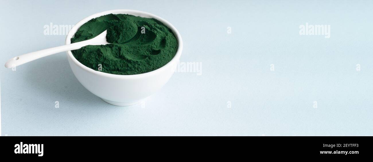 Bannière Spiruline poudre dans un bol blanc avec une cuillère à café sur fond bleu avec place pour le texte. Concept d'alimentation saine. Orientation horizontale. Banque D'Images