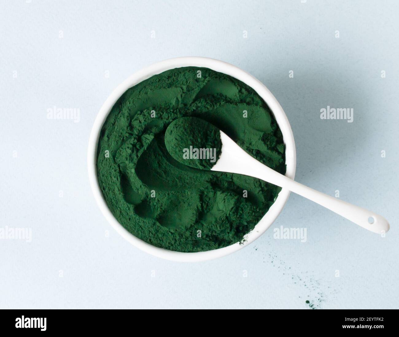 Poudre de chlorelle dans un bol blanc avec une cuillère à café sur fond bleu. Concept de super-alimentation. Orientation horizontale. Vue de dessus. Banque D'Images