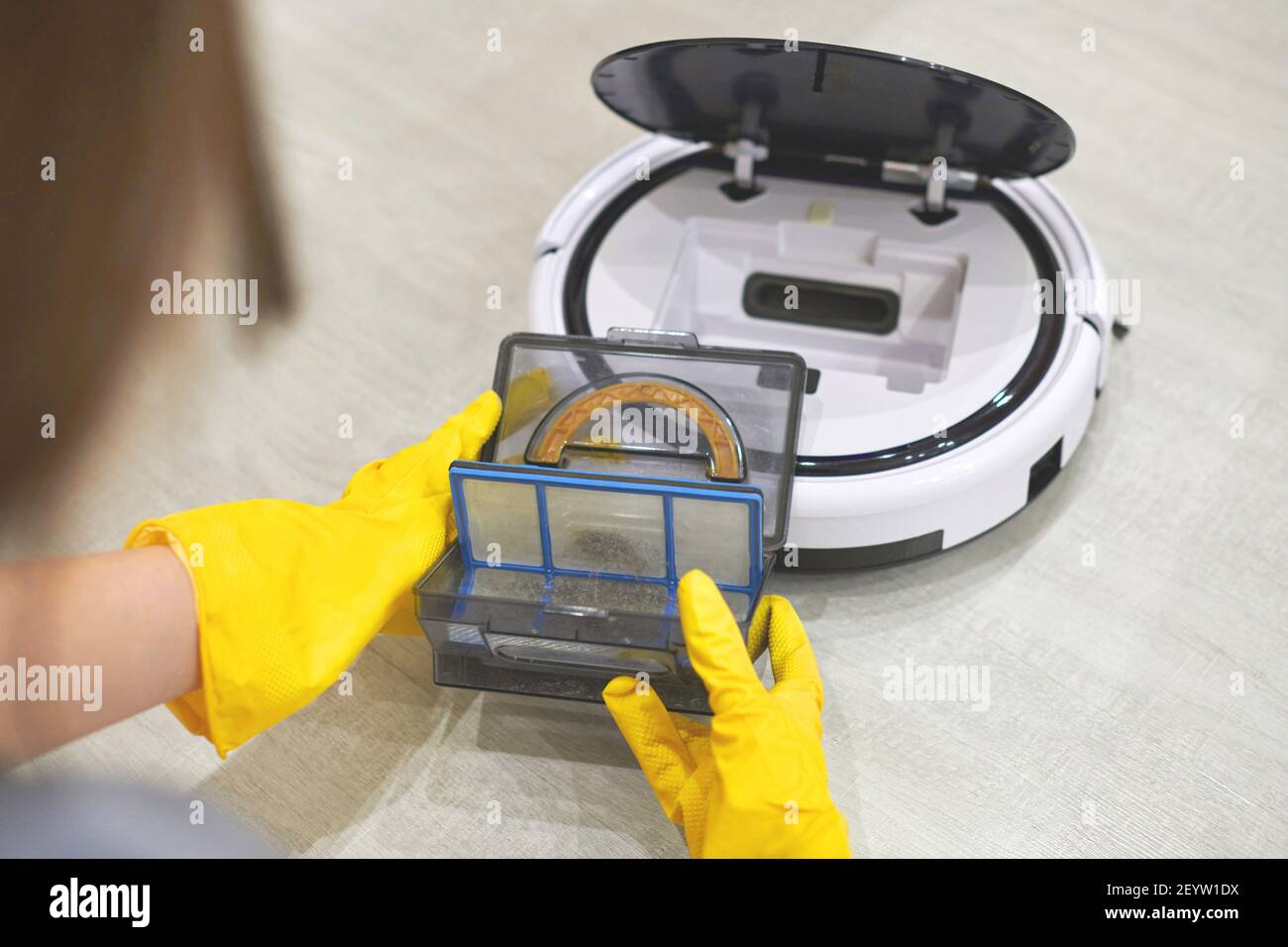 Boîte de rangement à poussière boîte d'aspirateur robotique à mains féminines gantées. Femme dans des gants de protection en sortant le récipient et le filtre pour le nettoyer de di Banque D'Images