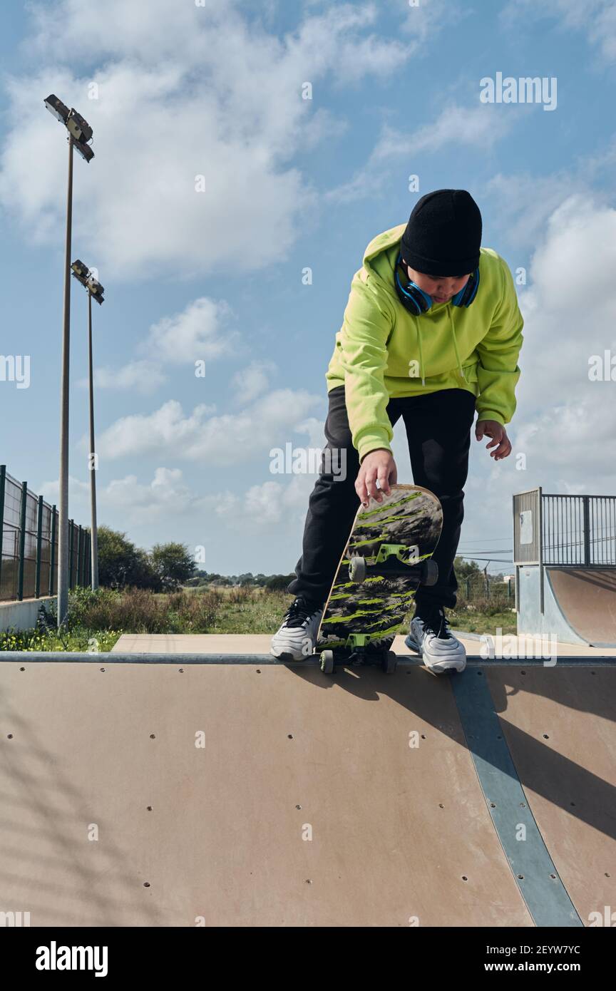 jeune, adolescent, avec une planche à roulettes, tenant la planche avec la main, pour lancer la pente, sur une piste, skateboard, portant des écouteurs, vert sw Banque D'Images