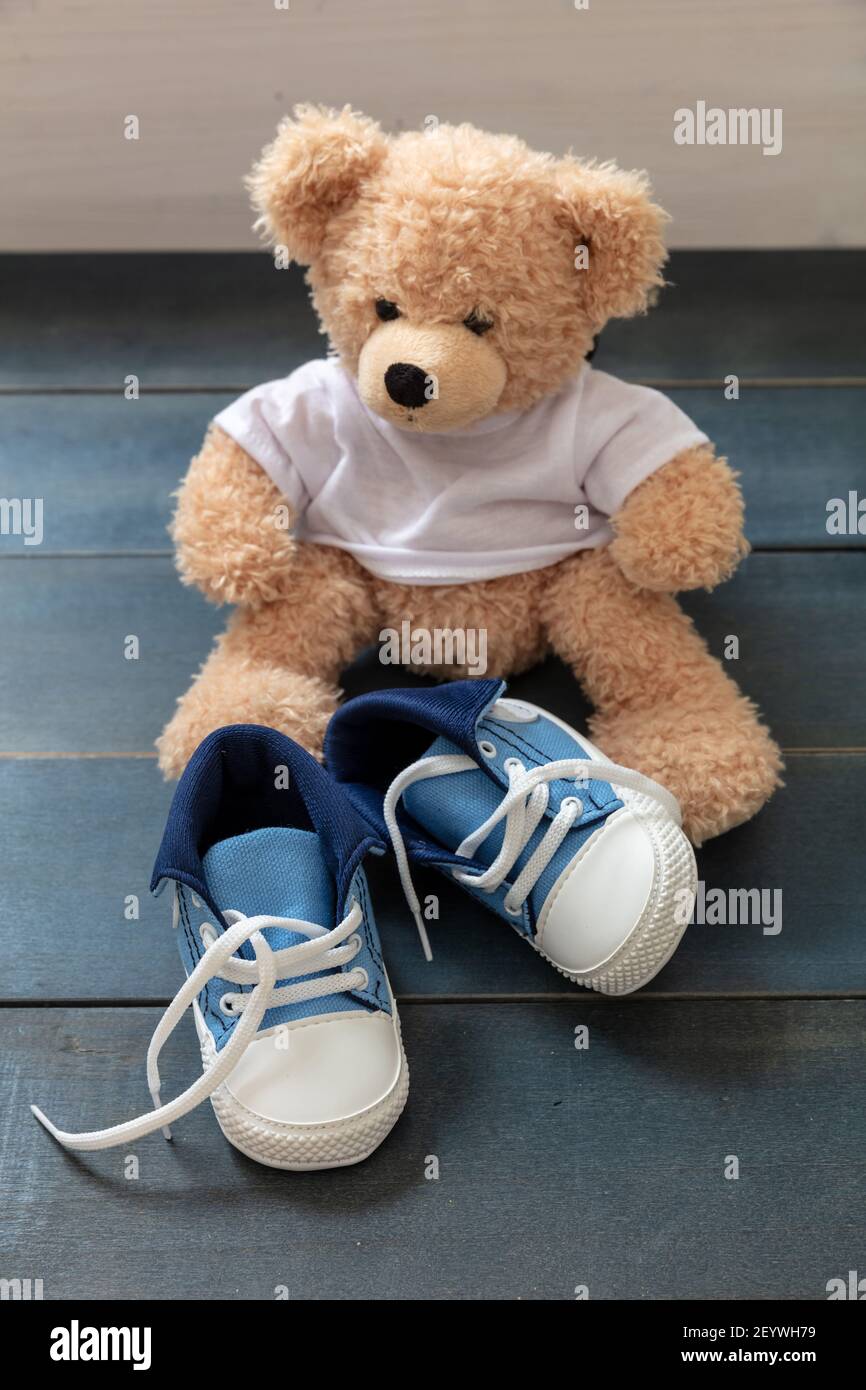 Baskets de petite taille pour enfant, chaussons en toile bleu et blanc avec  lacets pour chaussures dénoués. Chaussures de sport pour bébé et un  adorable ours en peluche sur parquet bleu Photo