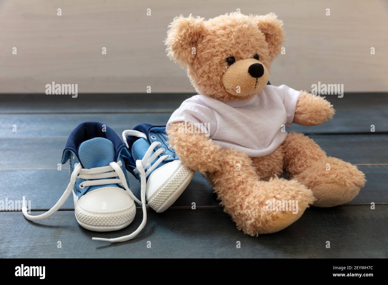 Chaussures de sport pour bébé et un adorable ours en peluche sur parquet  bleu. Baskets de petite taille pour enfant, chaussons en toile bleu et  blanc avec lacets pour chaussures dénoués Photo