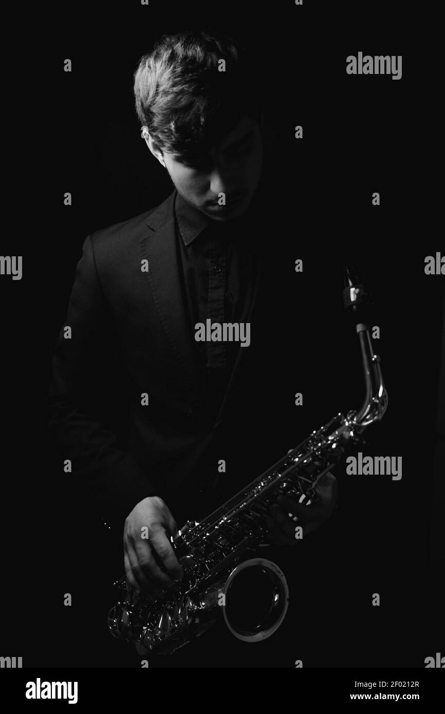 Une photo en niveaux de gris d'un homme sympa et charmant tenant son saxophone sur fond sombre Banque D'Images