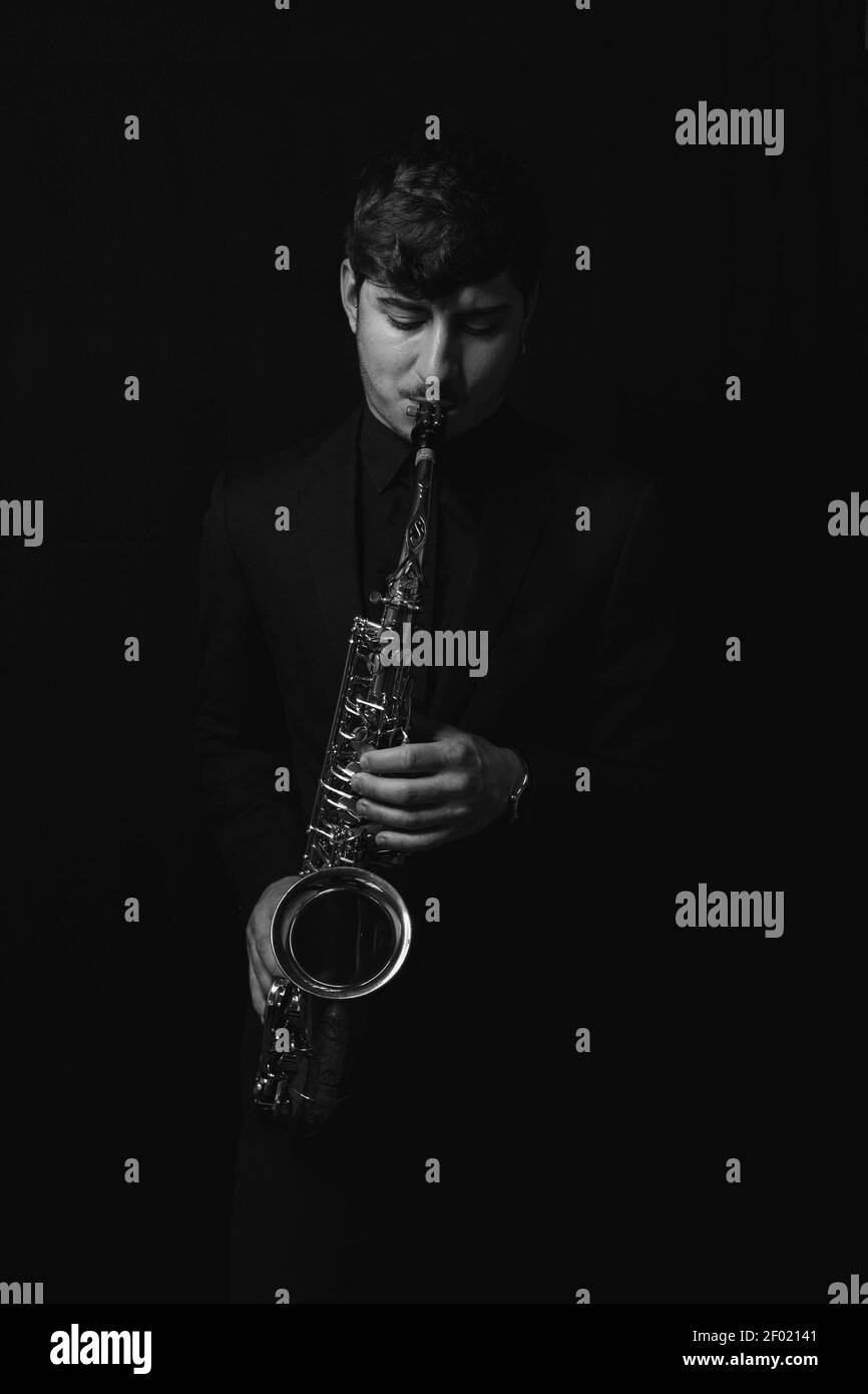 Une photo en niveaux de gris d'un gars sympa et sympathique jouant son saxophone isolé sur fond sombre Banque D'Images