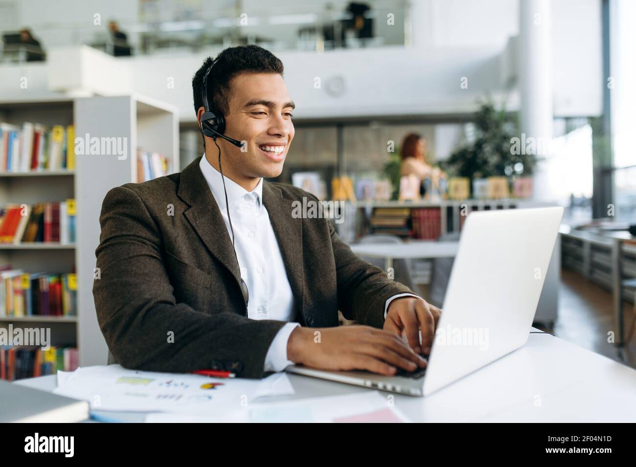 Homme d'affaires amical ou indépendant dans le casque, communique par appel vidéo. Un Manager ou un consultant professionnel séduisant s'assoit au bureau moderne avec un ordinateur portable, discutant en ligne Banque D'Images