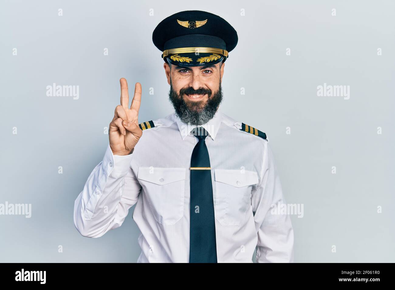 Jeune homme hispanique portant l'uniforme de pilote d'avion montrant et pointant avec les doigts numéro deux tout en souriant confiant et heureux. Banque D'Images