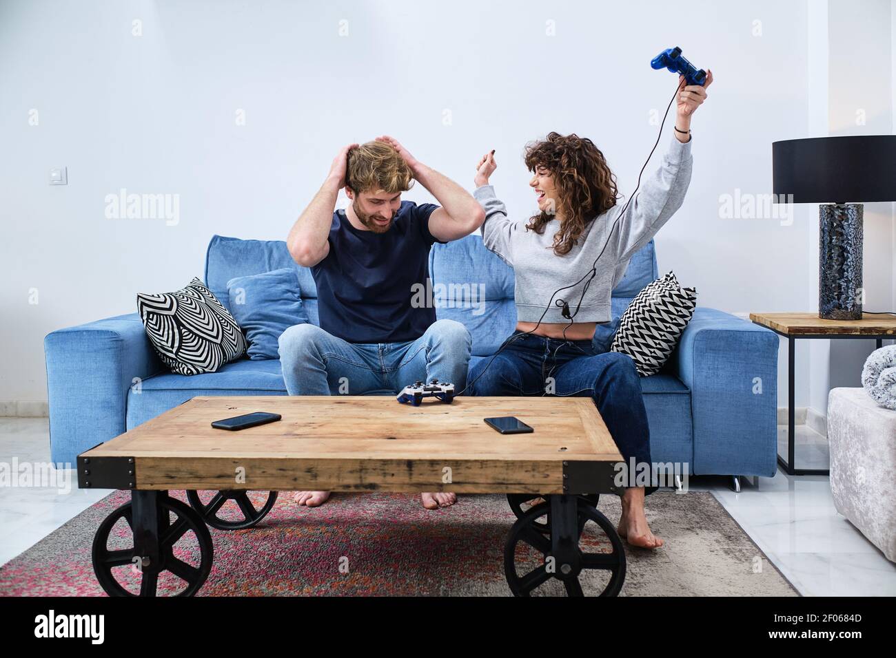 Jeune couple joyeux et excité dans des vêtements décontractés jouant la vidéo jeu sur console dans un salon élégant Banque D'Images