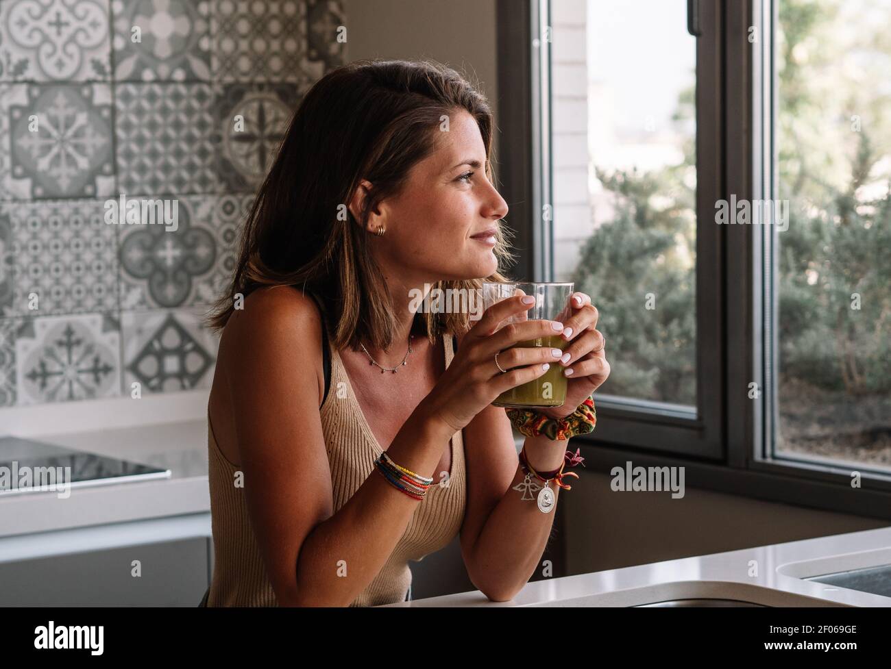 Caucasian girl est d'avoir un jus de légumes verts en face de sa grande fenêtre de cuisine Banque D'Images