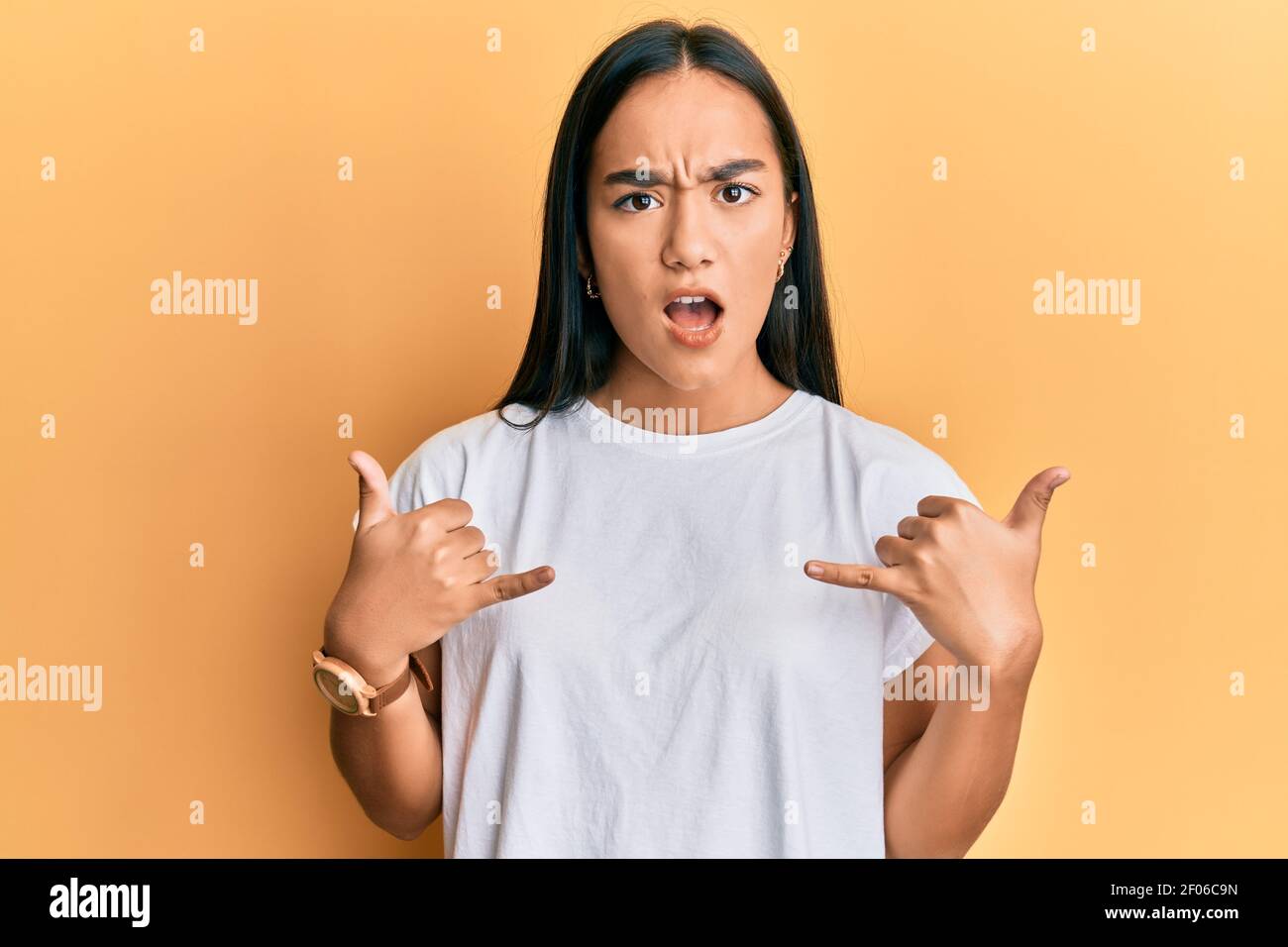 Jeune femme asiatique faisant le signe de shaka avec les mains dans le visage de choc, regardant sceptique et sarcastique, surpris par la bouche ouverte Banque D'Images